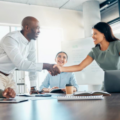 Two people in an office handshaking over a conference table